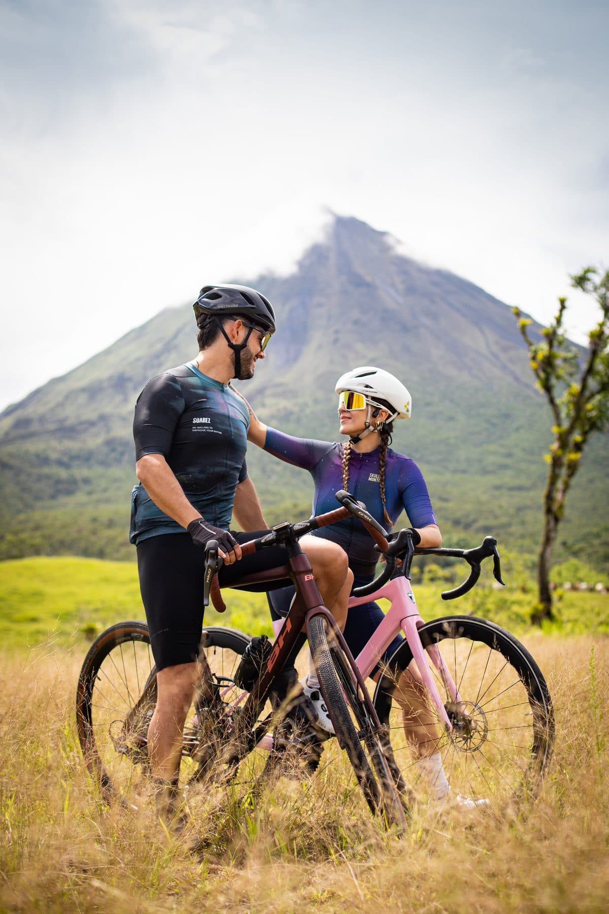 Dos ciclistas conversando en un potrero con el Volcán Arenal detrás
