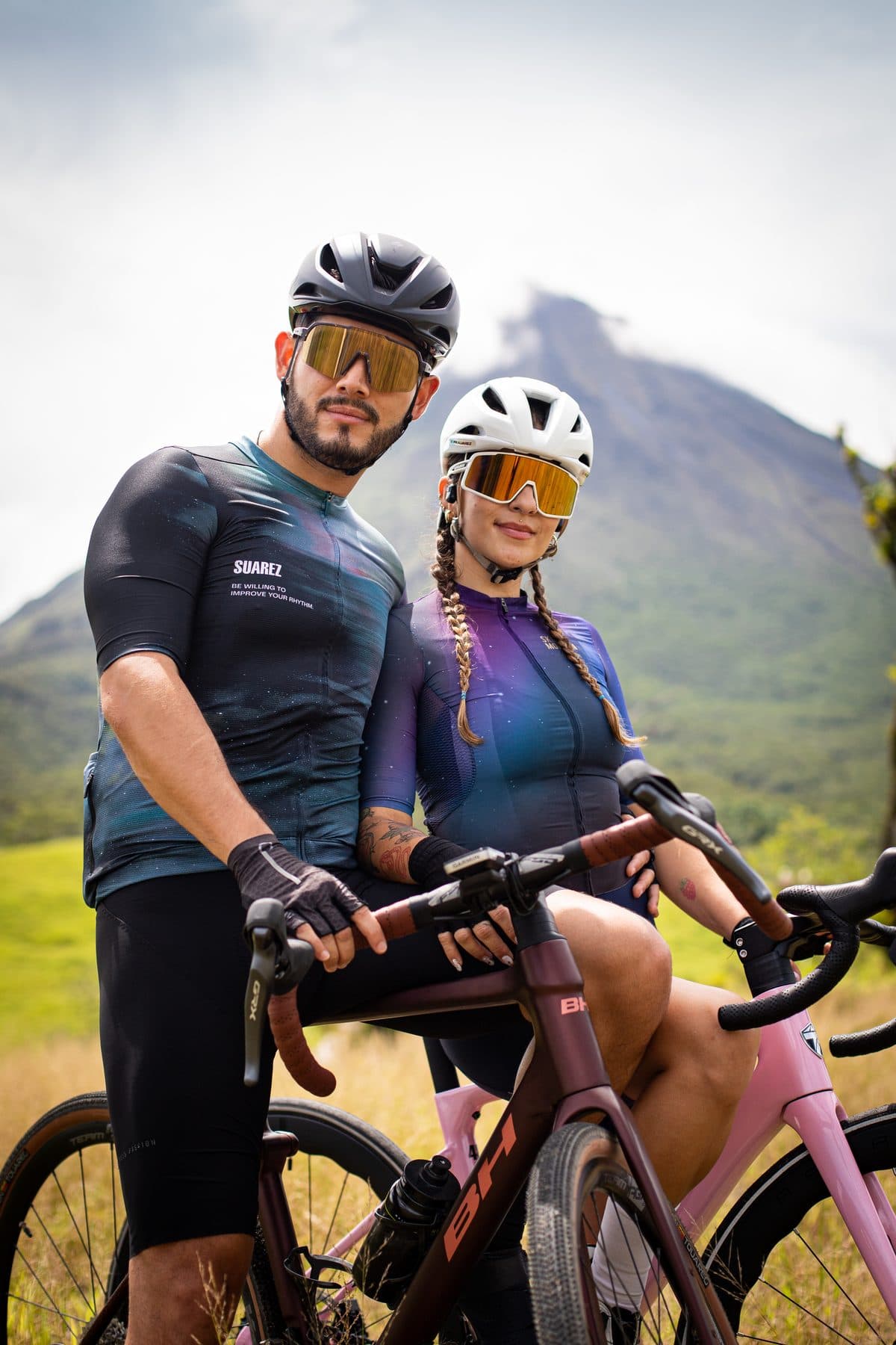 Pareja de ciclistas apoyada en su bicicleta frente al Volcán Arenal