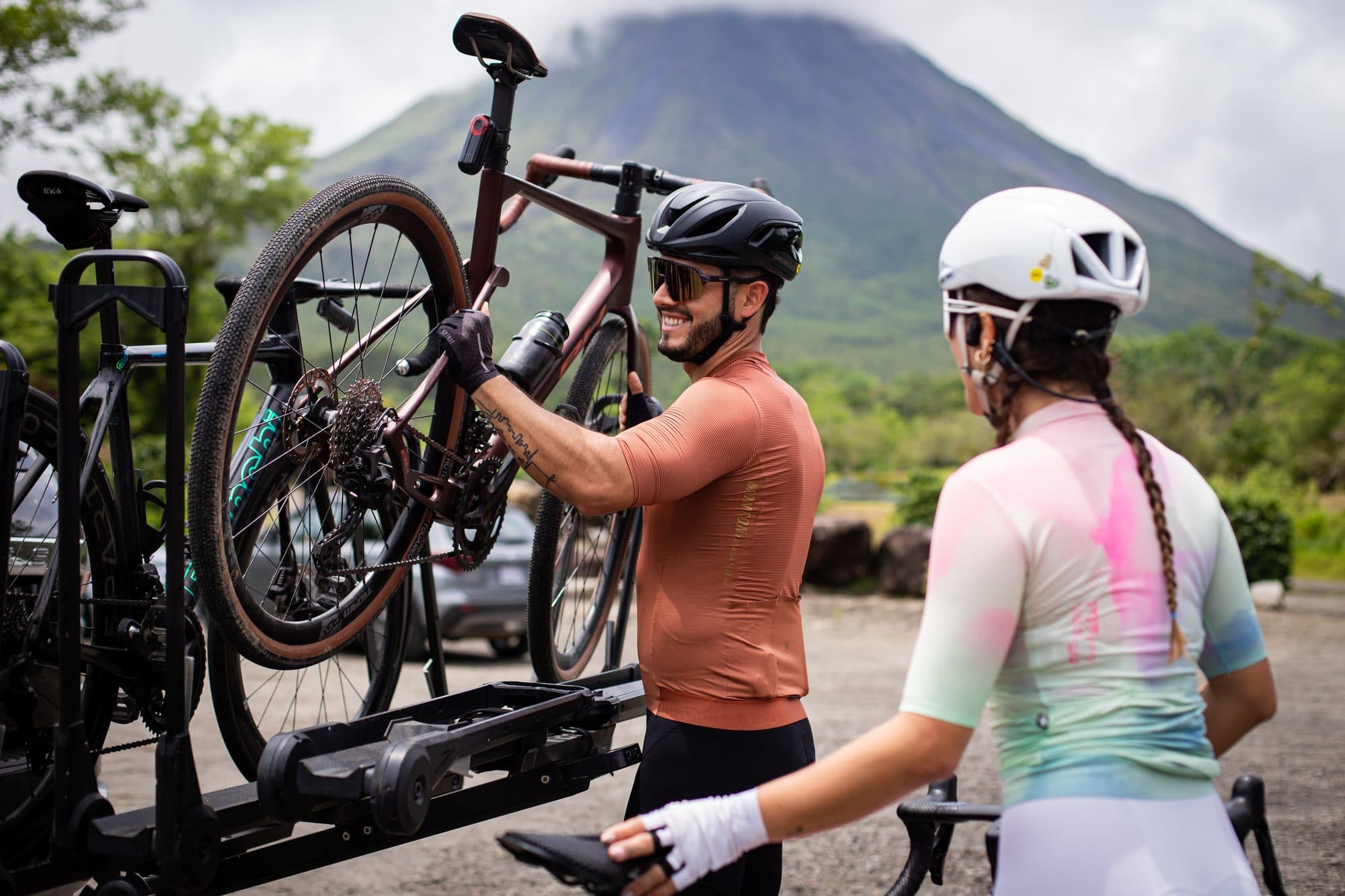 Dos ciclistas bajando las bicicletas del portabicicletas con el Volcán Arenal de fondo